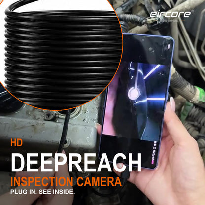 A hand feeding the DeepReach probe into a valve-cover port on a dirty engine while the phone beside it shows the lit view from inside