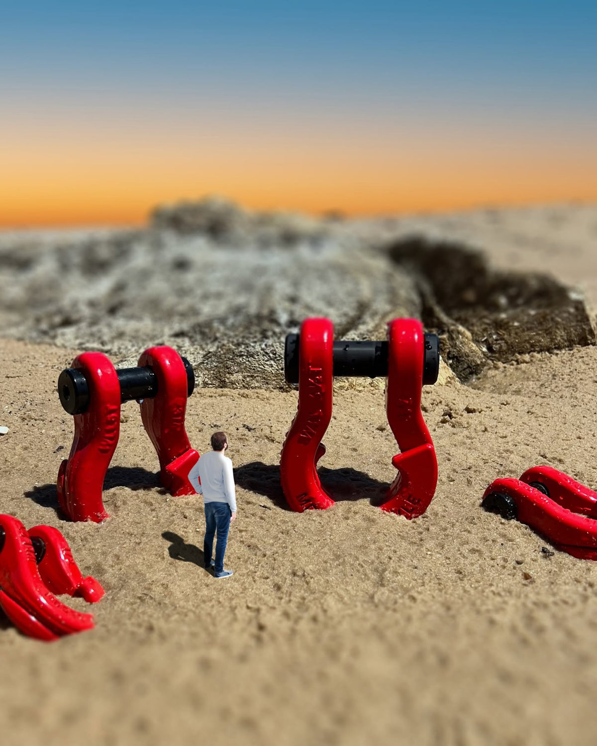 Oversized D-ring shackles on sand at sunset, shown at exaggerated scale